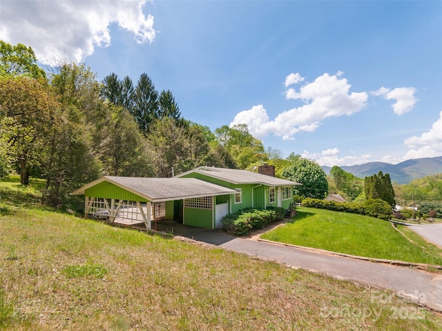 ranch-style home featuring aphalt driveway, a chimney, a front yard, and a carport