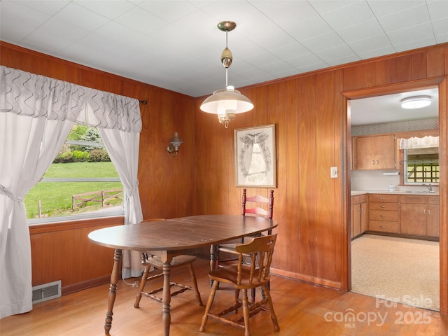 dining area featuring baseboards, light wood-type flooring, wood walls, and visible vents