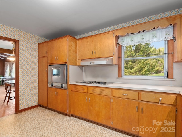 kitchen with under cabinet range hood, wallpapered walls, stainless steel oven, and light countertops
