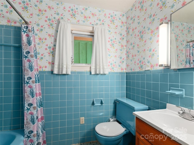 bathroom with wainscoting, vanity, toilet, wallpapered walls, and tile walls