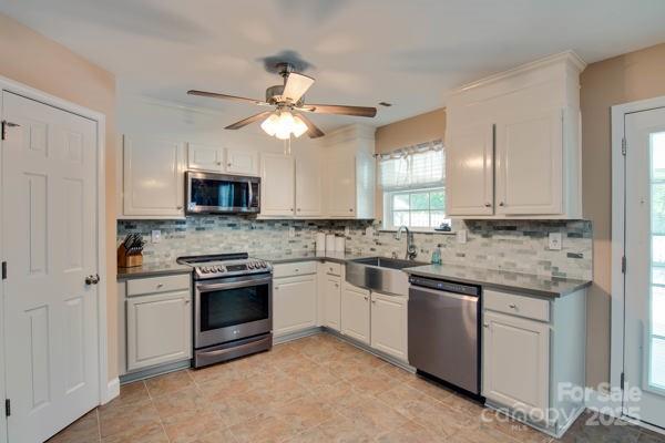 136 Elba Dr, Mooresville, NC 28115 - kitchen featuring stainless steel appliances, backsplash, white cabinetry, a ceiling fan, and dark countertops
