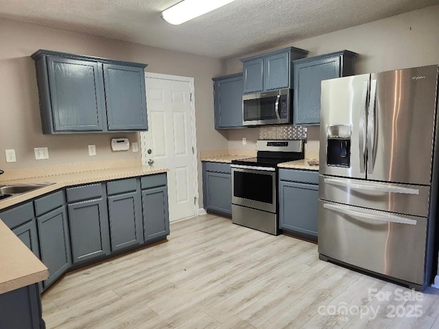 kitchen featuring appliances with stainless steel finishes, light wood-style flooring, light countertops, a textured ceiling, and a sink