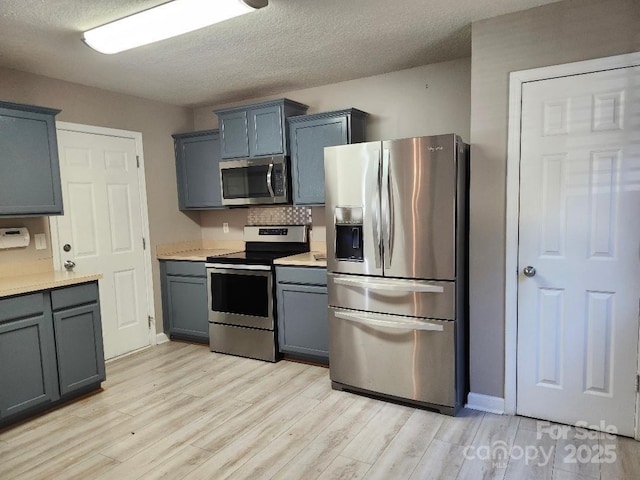kitchen featuring stainless steel appliances, light wood-type flooring, light countertops, a textured ceiling, and baseboards
