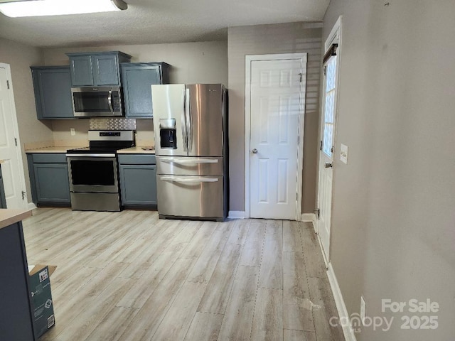 kitchen featuring stainless steel appliances, light wood finished floors, light countertops, and baseboards