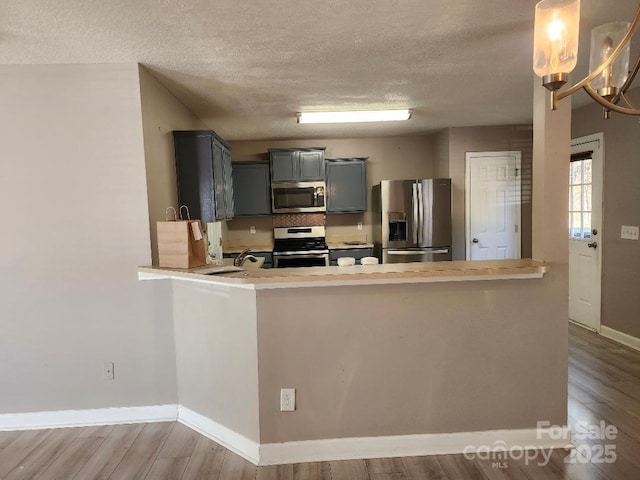 kitchen with appliances with stainless steel finishes, a textured ceiling, wood finished floors, baseboards, and a peninsula