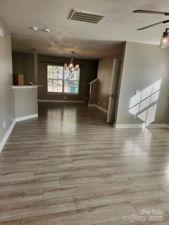 unfurnished room featuring a chandelier, a textured ceiling, baseboards, and wood finished floors