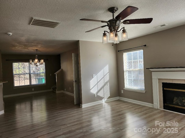 unfurnished living room featuring a textured ceiling, a chandelier, a tiled fireplace, wood finished floors, and healthy amount of natural light