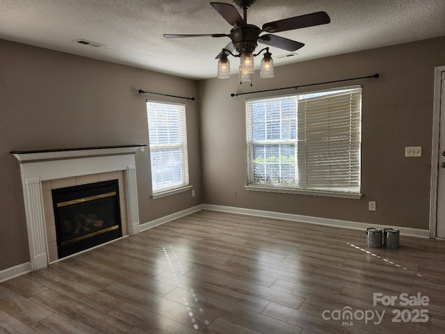 unfurnished living room featuring a ceiling fan, a textured ceiling, wood finished floors, a tiled fireplace, and baseboards