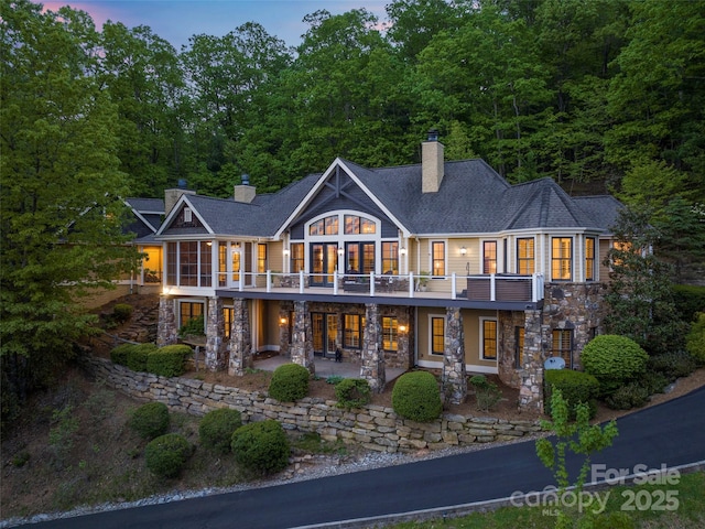 714 Wickhams Fancy Dr, Biltmore Lake, NC 28715 - back of house at dusk with a patio area, stone siding, a chimney, a sunroom, and a shingled roof