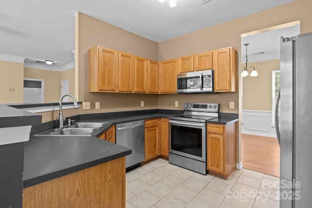 kitchen featuring dark countertops, a sink, stainless steel appliances, a peninsula, and ornamental molding
