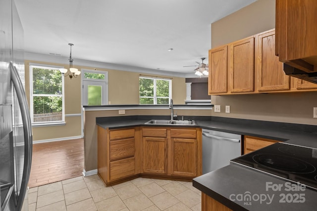 kitchen with appliances with stainless steel finishes, dark countertops, a sink, ceiling fan with notable chandelier, and a peninsula