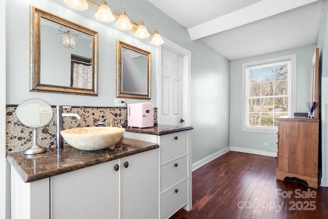 bathroom featuring vanity, baseboards, decorative backsplash, wood finished floors, and beamed ceiling