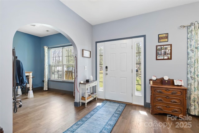 entryway with arched walkways, baseboards, and wood finished floors