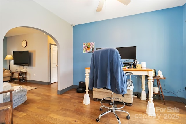 office space featuring baseboards, arched walkways, ceiling fan, and wood finished floors