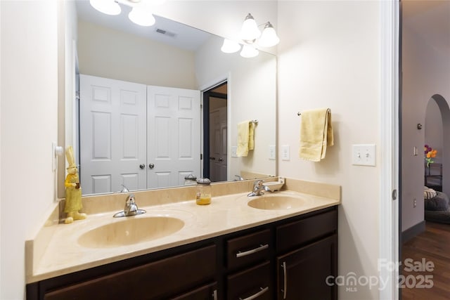 full bath with double vanity, visible vents, a sink, and wood finished floors