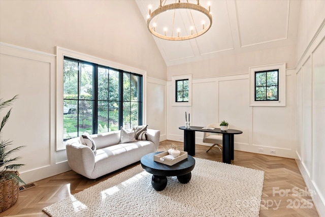 living area with high vaulted ceiling, a notable chandelier, a decorative wall, and visible vents
