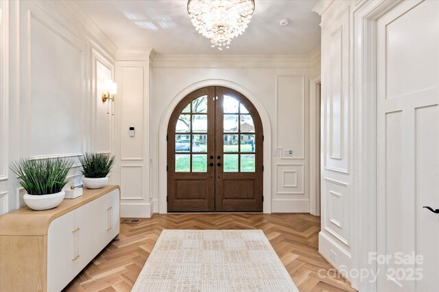 entryway with french doors, arched walkways, a chandelier, ornamental molding, and a decorative wall
