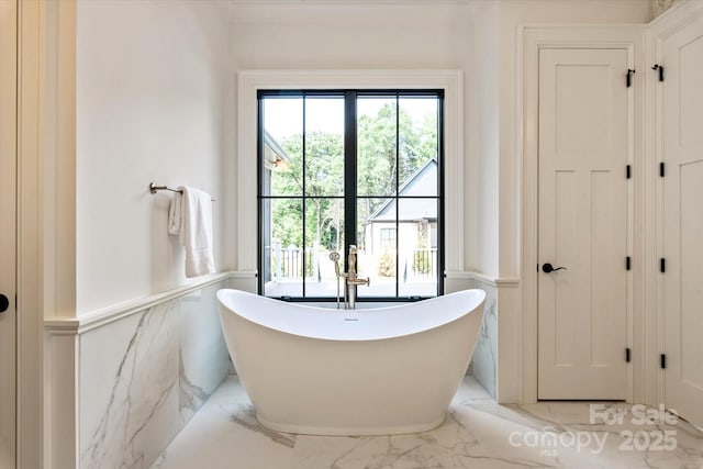 bathroom featuring marble finish floor, wainscoting, and a soaking tub