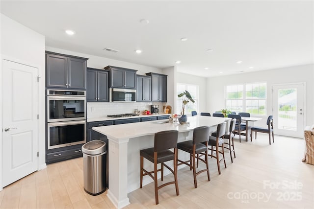 4069 Havenport Cir, Tega Cay, SC 29708 - kitchen featuring appliances with stainless steel finishes, an island with sink, a kitchen bar, backsplash, and light wood-style floors
