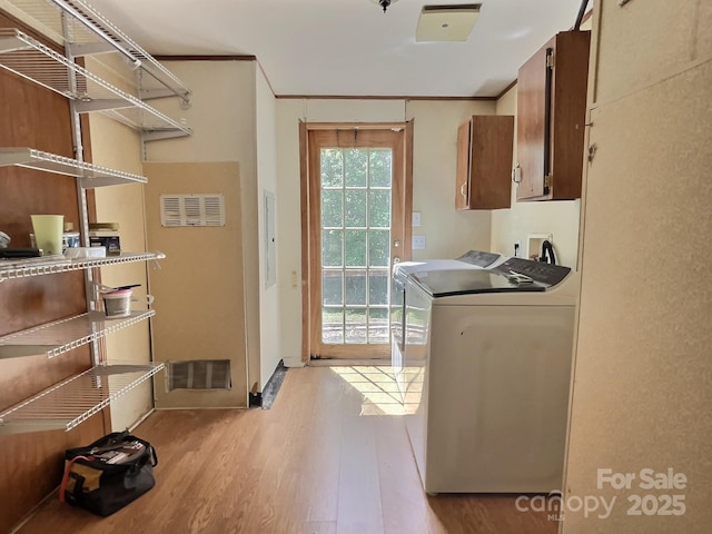laundry area with light wood-style flooring, cabinet space, washer and clothes dryer, and ornamental molding