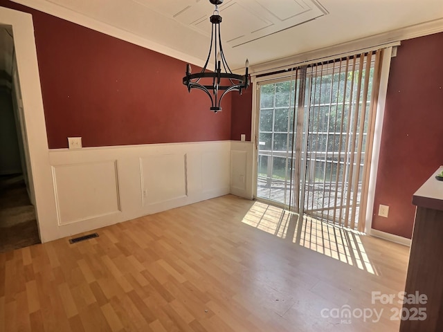 unfurnished dining area with visible vents, wainscoting, wood finished floors, an inviting chandelier, and a decorative wall