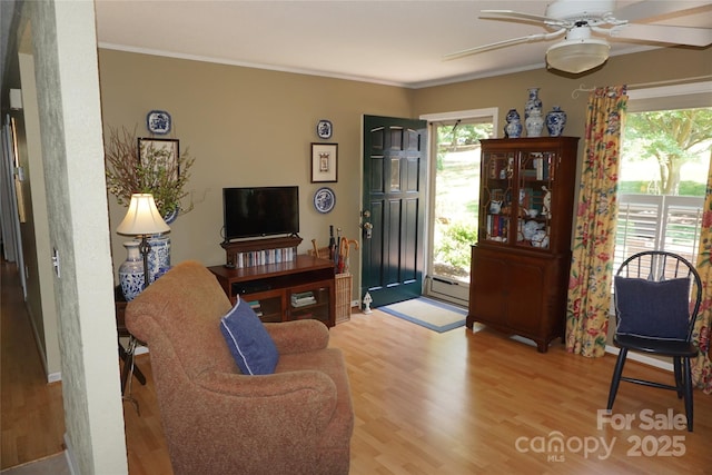 living room with ornamental molding, light wood-style flooring, ceiling fan, and a baseboard heating unit