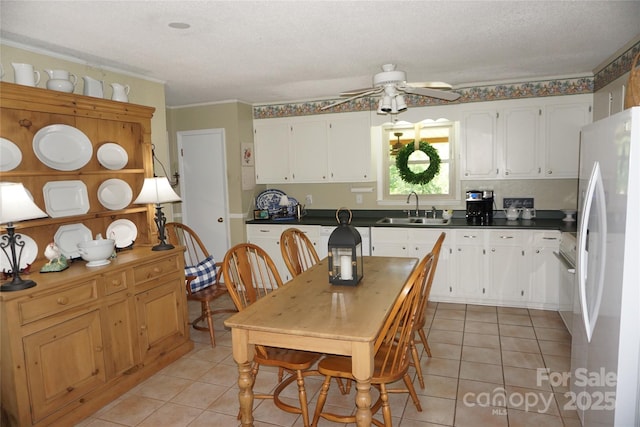kitchen featuring a ceiling fan, dark countertops, a sink, freestanding refrigerator, and light tile patterned flooring