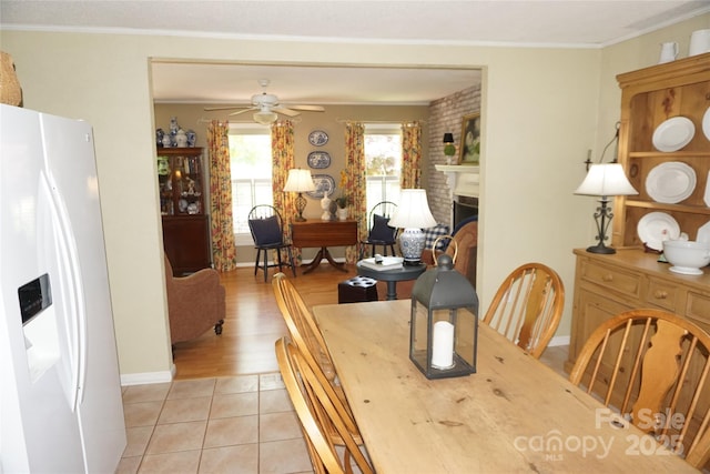 dining room with crown molding, light tile patterned flooring, ceiling fan, a brick fireplace, and baseboards