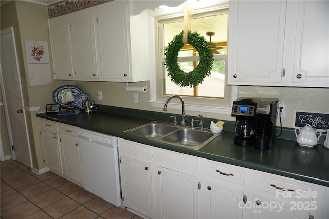 kitchen featuring white dishwasher, dark countertops, a sink, white cabinets, and light tile patterned flooring