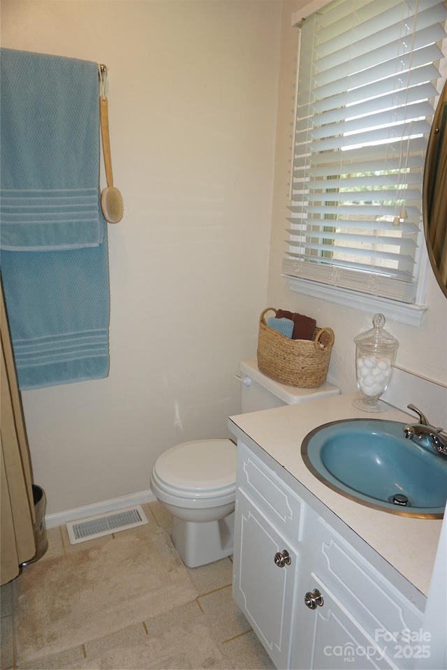half bathroom with tile patterned flooring, vanity, toilet, baseboards, and visible vents
