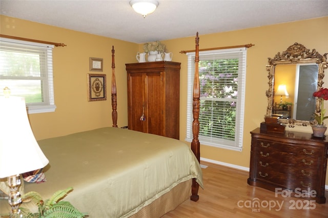 bedroom with baseboards, multiple windows, and wood finished floors