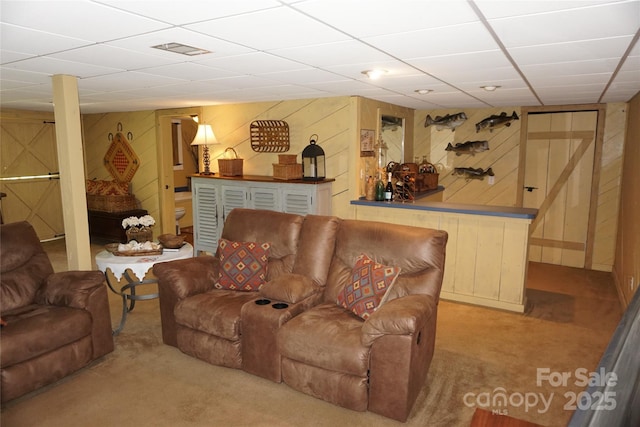 living area with visible vents, wood walls, a paneled ceiling, and carpet