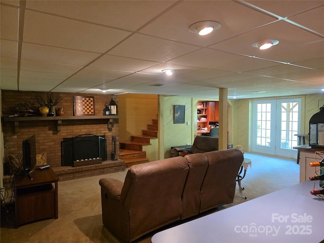 carpeted living room featuring a brick fireplace, a drop ceiling, and stairs