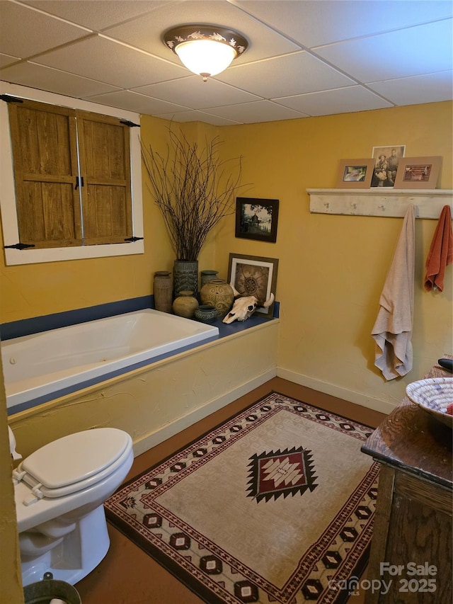 bathroom featuring toilet, baseboards, a drop ceiling, and a tub to relax in