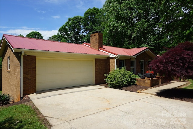 ranch-style home featuring metal roof, a chimney, a garage, brick siding, and concrete driveway