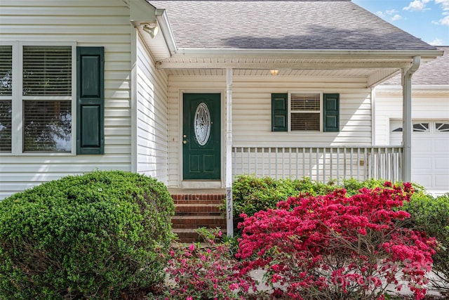 entrance to property with covered porch, an attached garage, and a shingled roof