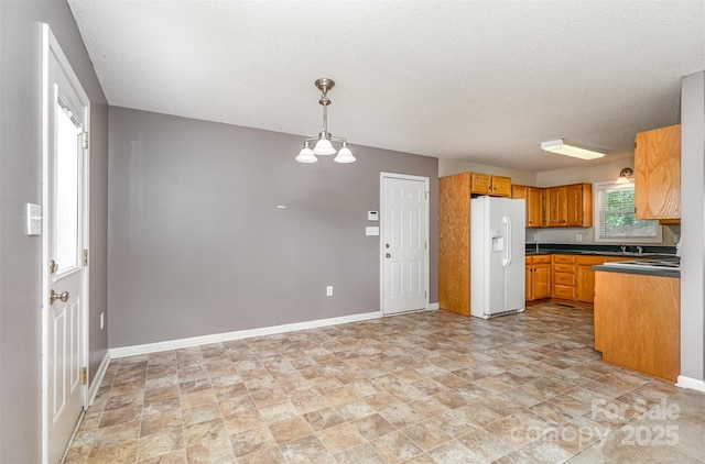 kitchen with dark countertops, white fridge with ice dispenser, stone finish flooring, and a textured ceiling