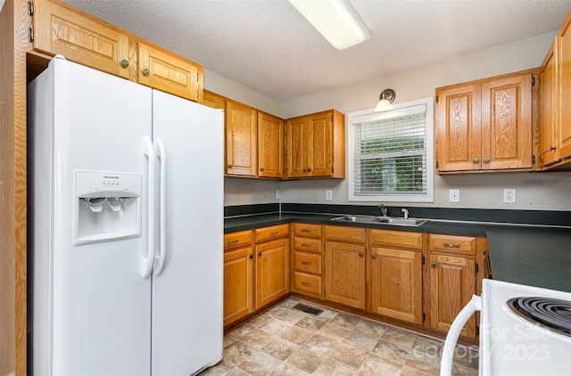 kitchen with visible vents, dark countertops, brown cabinets, a sink, and white appliances