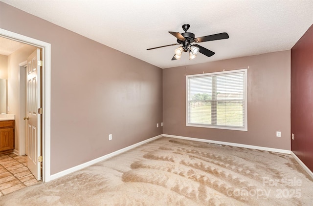 unfurnished room featuring a ceiling fan, baseboards, and light carpet