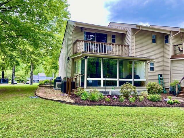 back of property with a balcony, a yard, and a sunroom