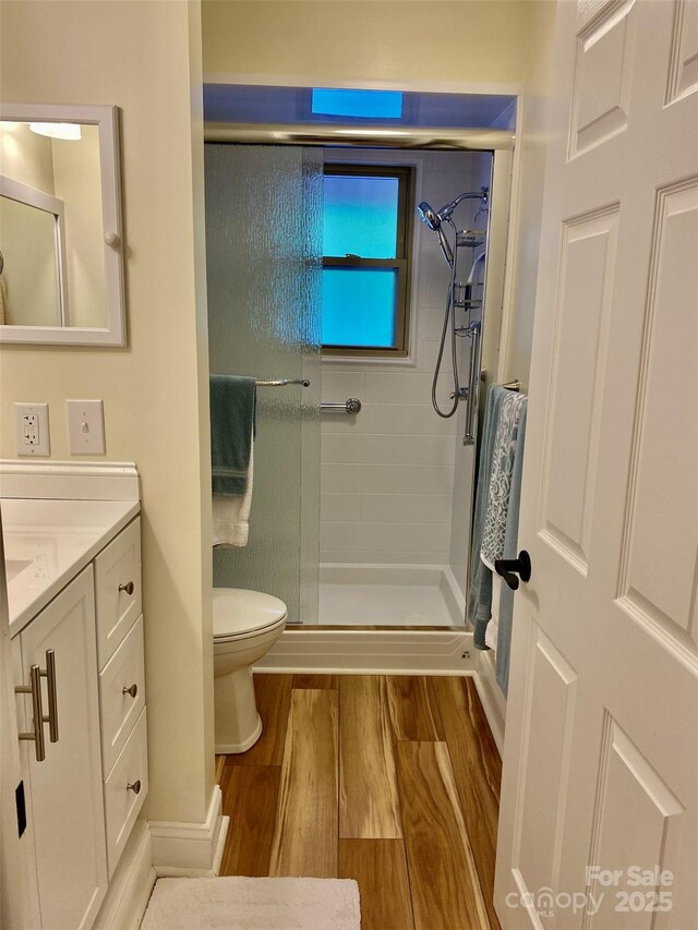 bathroom featuring a shower stall, toilet, wood finished floors, and vanity