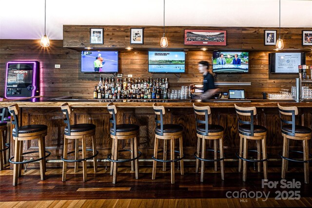 indoor wet bar with wooden walls, hanging light fixtures, and wood-type flooring