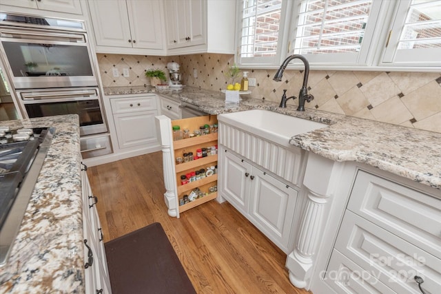 12048 Royal Portrush Dr, Charlotte, NC 28277 - kitchen with white cabinetry, stainless steel double oven, a sink, and light wood-style floors