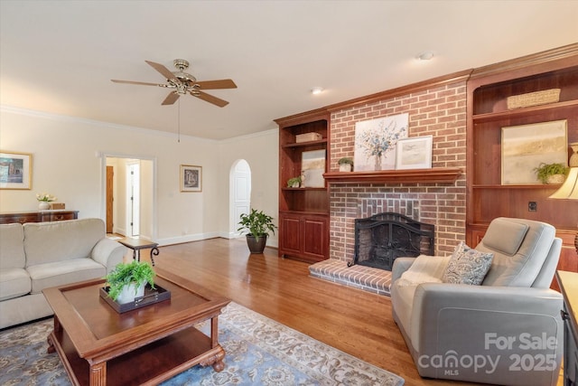 12048 Royal Portrush Dr, Charlotte, NC 28277 - living room featuring a ceiling fan, arched walkways, a fireplace, built in shelves, and wood finished floors