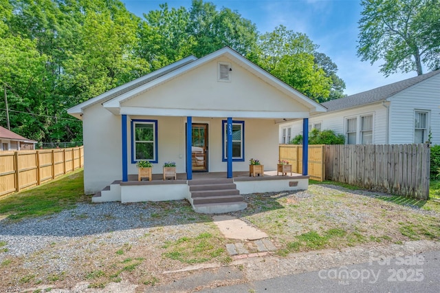 bungalow with a porch, stucco siding, and fence