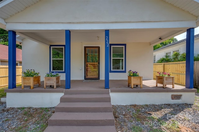 entrance to property with a porch, fence, and stucco siding