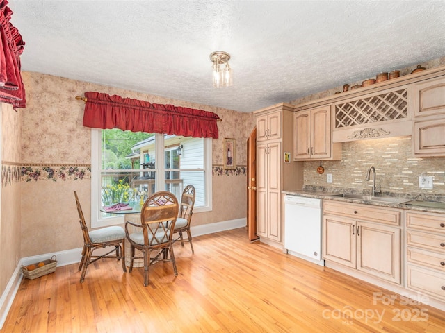 kitchen featuring a textured ceiling, dishwasher, baseboards, a sink, and light wood-style floors