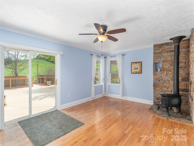 unfurnished living room with a textured ceiling, baseboards, light wood finished floors, ceiling fan, and a wood stove