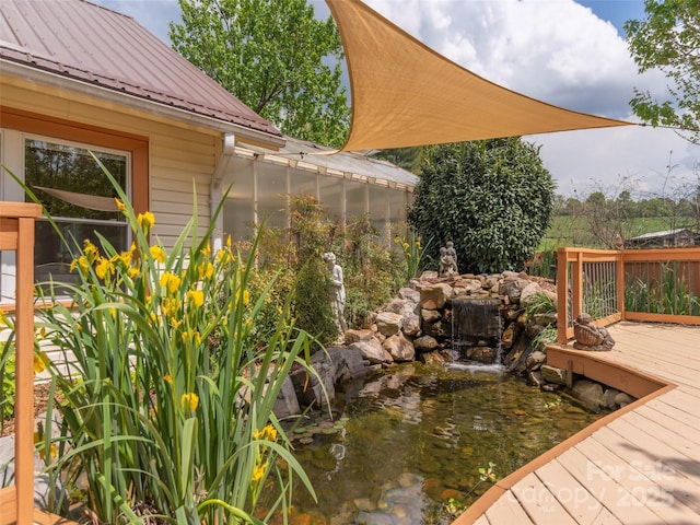 view of yard featuring a deck, a greenhouse, and a small pond