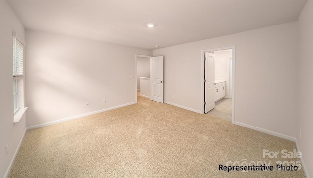 unfurnished bedroom featuring light colored carpet, baseboards, and ensuite bath